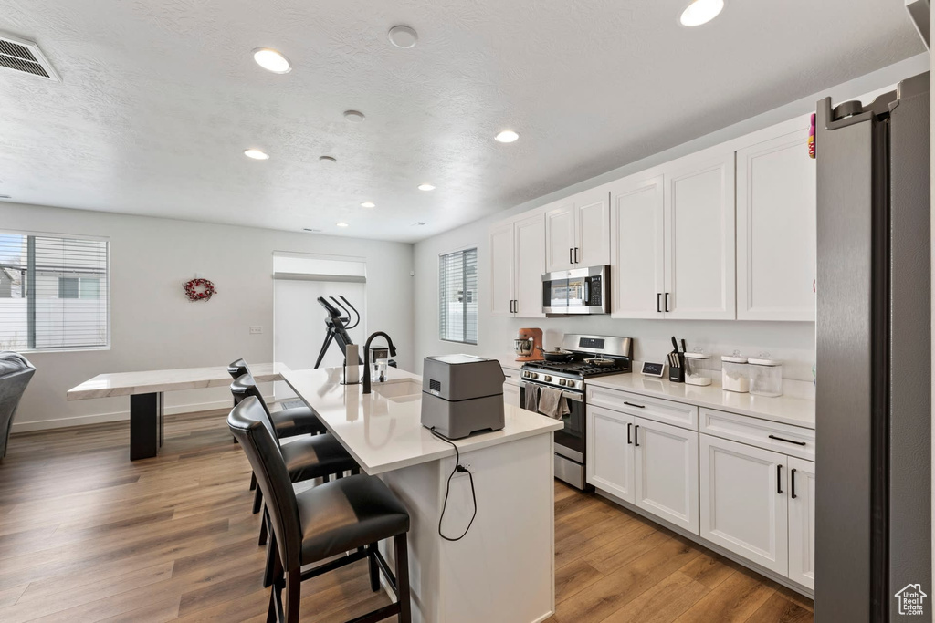 Kitchen featuring appliances with stainless steel finishes, light wood-type flooring, a breakfast bar area, and white cabinets