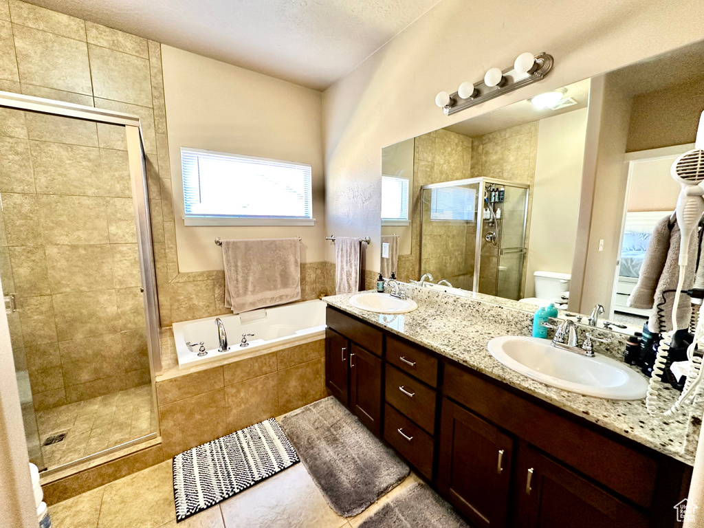 Full bathroom with dual sinks, tile flooring, plus walk in shower, and vanity with extensive cabinet space