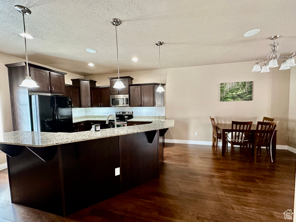 Kitchen featuring stainless steel appliances, dark hardwood / wood-style flooring, light stone counters, dark brown cabinets, and pendant lighting