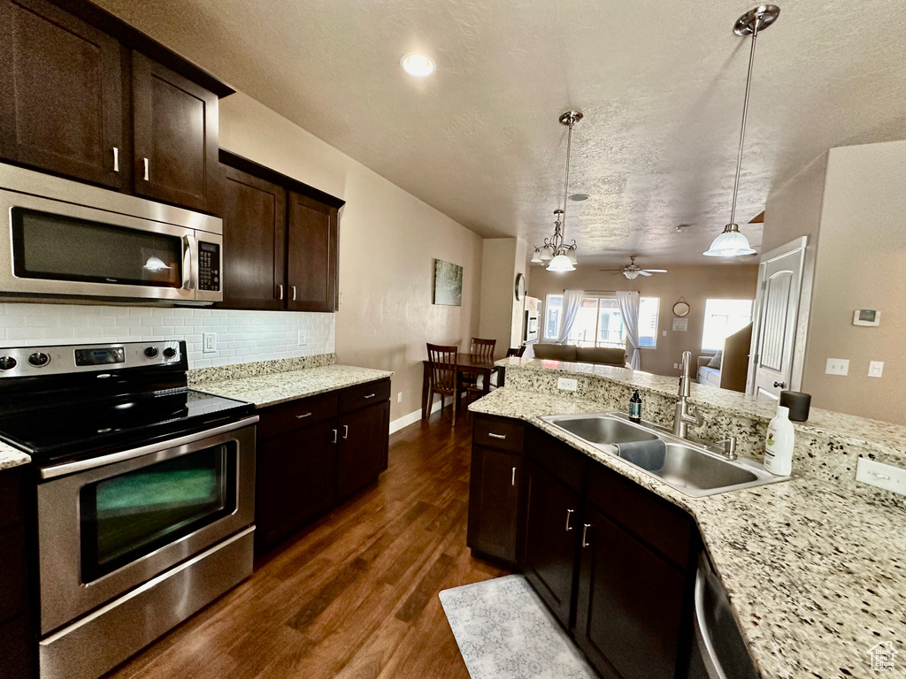 Kitchen featuring stainless steel appliances, dark hardwood / wood-style floors, sink, ceiling fan with notable chandelier, and decorative light fixtures