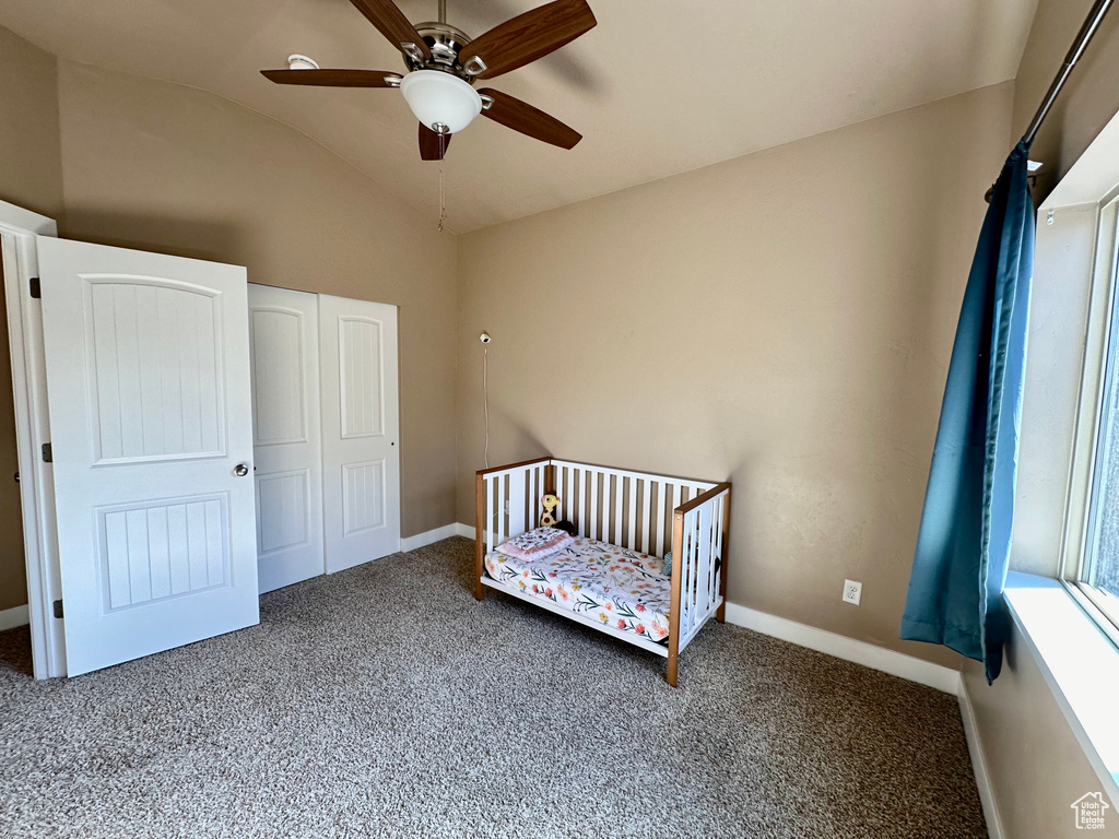 Unfurnished bedroom featuring a closet, ceiling fan, a nursery area, lofted ceiling, and dark colored carpet