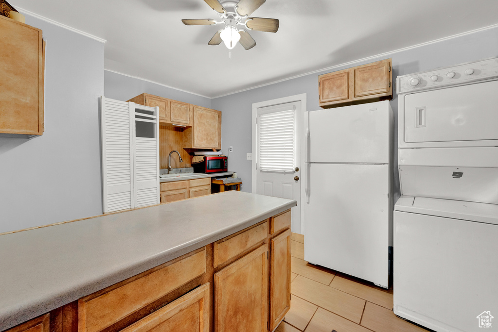 Kitchen featuring light tile flooring, ceiling fan, sink, white fridge, and stacked washer and dryer