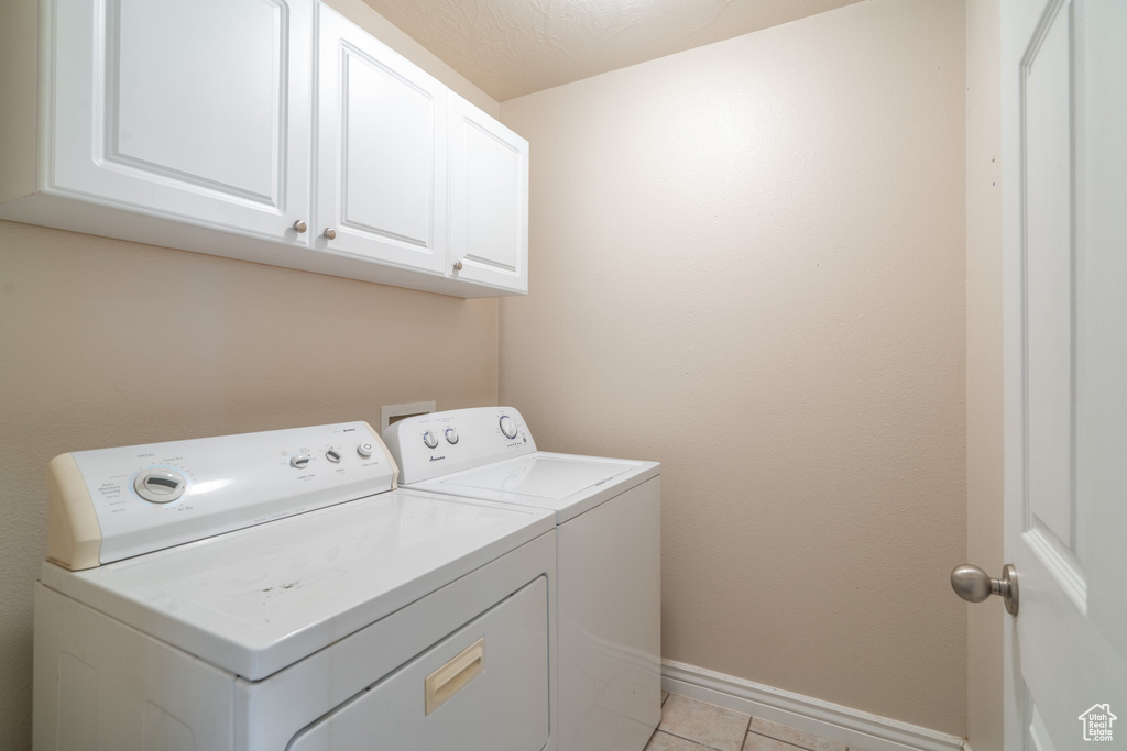Laundry room with washing machine and dryer, light tile floors, and cabinets