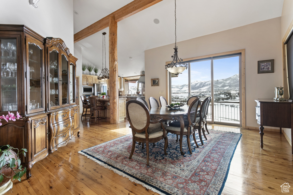 Dining room with a healthy amount of sunlight, light hardwood / wood-style floors, a mountain view, and high vaulted ceiling