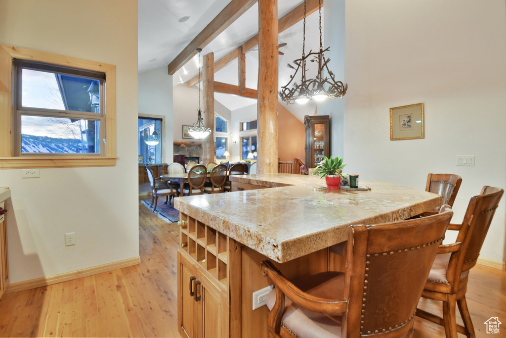 Kitchen with a notable chandelier, light stone countertops, light hardwood / wood-style flooring, hanging light fixtures, and a breakfast bar area