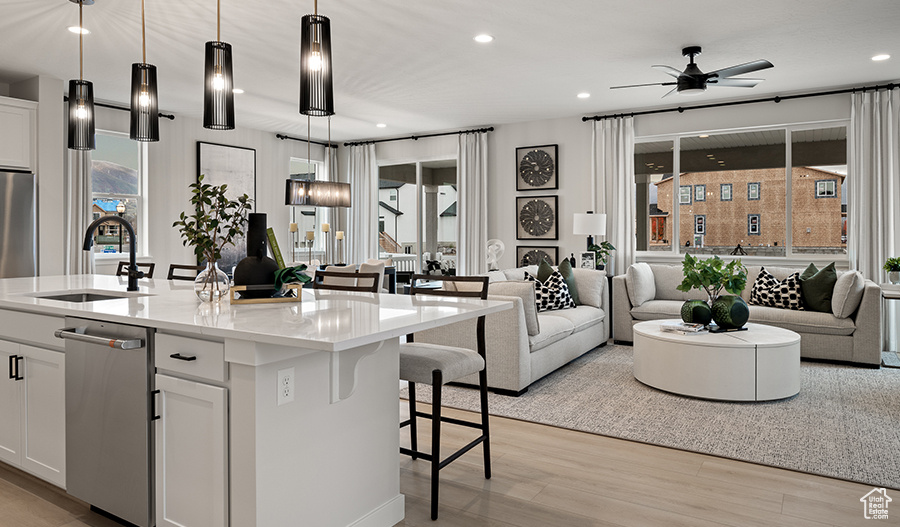 Interior space featuring white cabinetry, light hardwood / wood-style flooring, ceiling fan, a kitchen island with sink, and stainless steel dishwasher