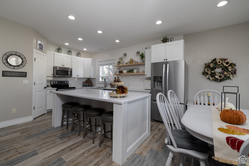 Kitchen featuring white cabinets, appliances with stainless steel finishes, tasteful backsplash, and hardwood / wood-style floors