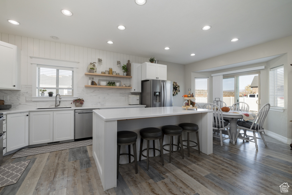 Kitchen featuring white cabinets, dark hardwood / wood-style flooring, backsplash, stainless steel appliances, and a breakfast bar area