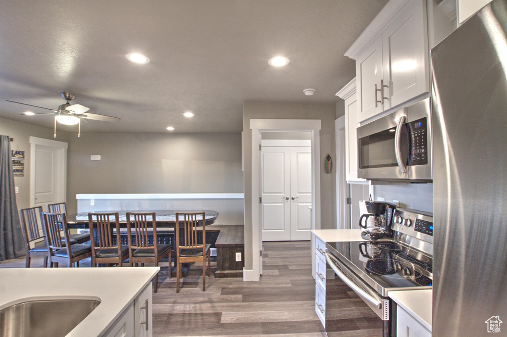 Kitchen with appliances with stainless steel finishes, white cabinets, dark wood-type flooring, and ceiling fan