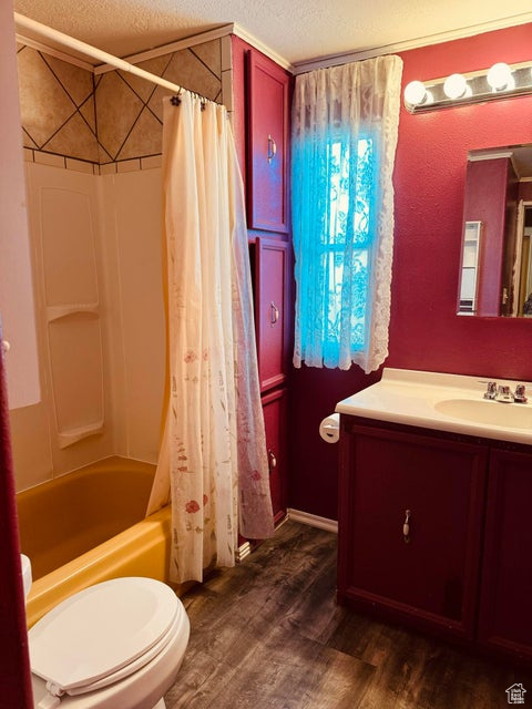 Full bathroom featuring hardwood / wood-style floors, shower / tub combo with curtain, a textured ceiling, toilet, and vanity