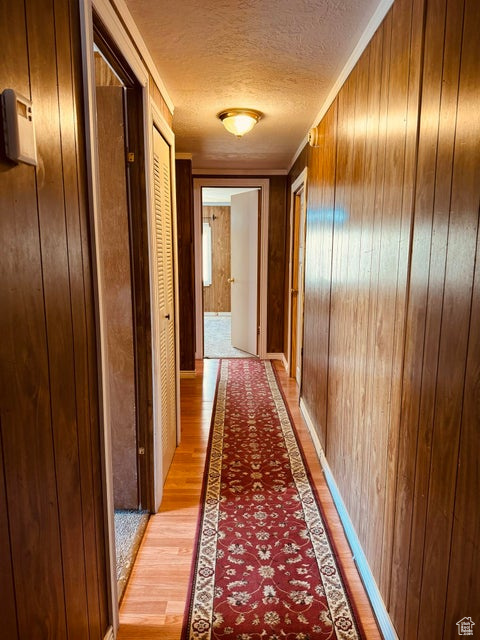Hall with ornamental molding, a textured ceiling, wood walls, and light hardwood / wood-style floors
