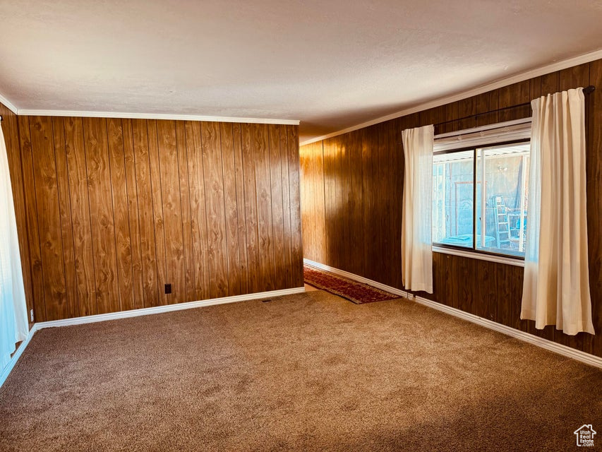 Unfurnished room with dark colored carpet, wood walls, and crown molding