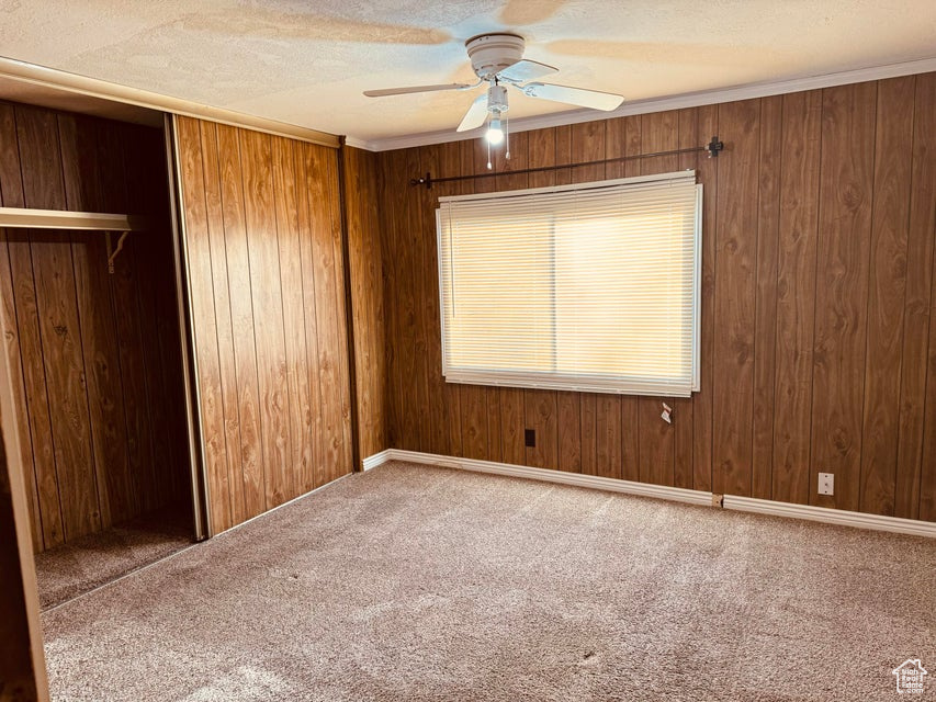 Unfurnished room with wood walls, carpet, ornamental molding, and ceiling fan