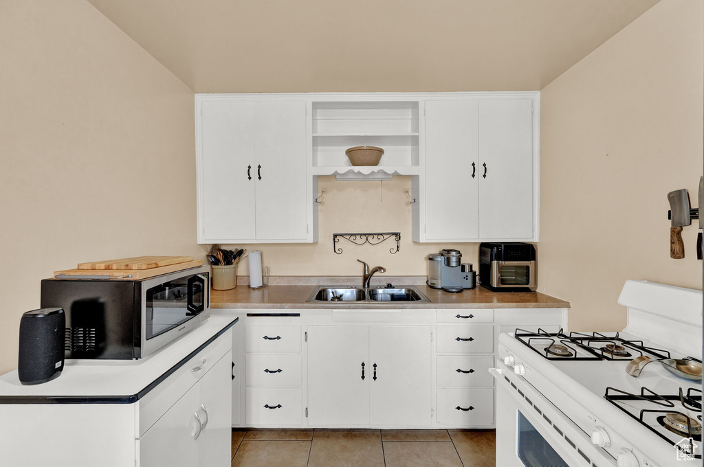 Kitchen featuring sink, white cabinetry, white gas range oven, and light tile floors