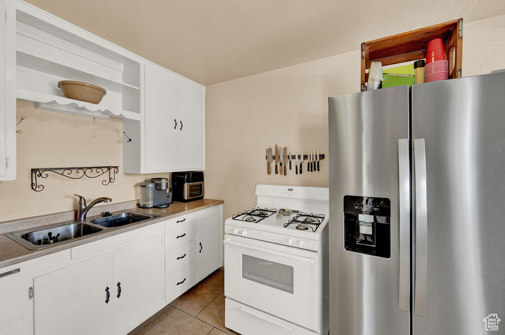 Kitchen with stainless steel fridge, white cabinetry, white range with gas stovetop, and sink