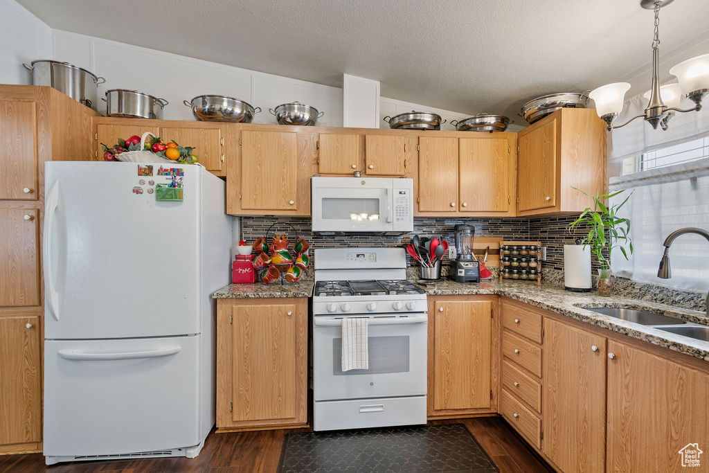 Kitchen with dark hardwood / wood-style flooring, white appliances, sink, backsplash, and an inviting chandelier