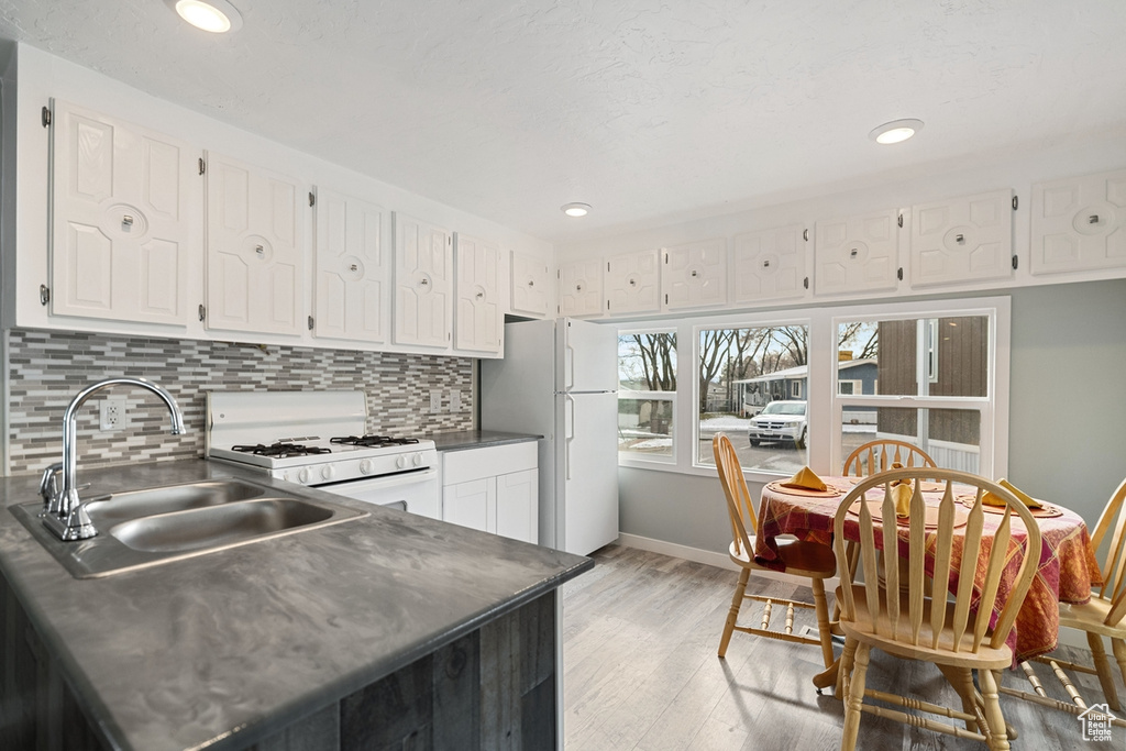 Kitchen with tasteful backsplash, white cabinets, white appliances, sink, and light hardwood / wood-style flooring