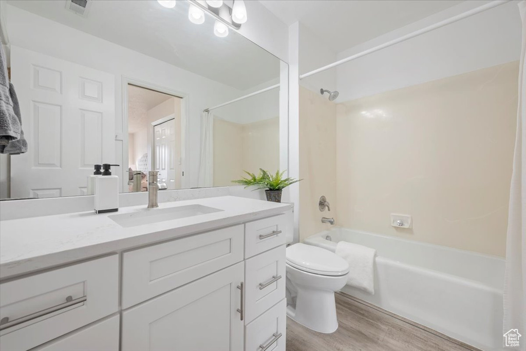 Full bathroom featuring hardwood / wood-style flooring, toilet, vanity with extensive cabinet space, and shower / bathtub combination with curtain