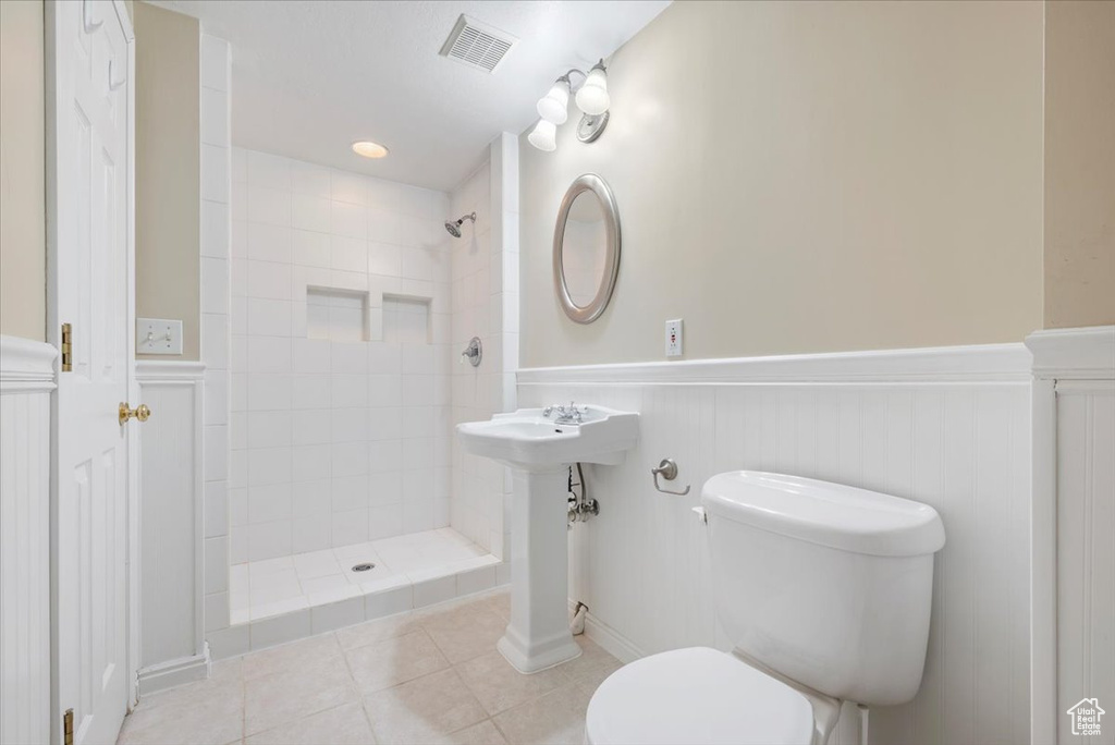 Bathroom with toilet, a tile shower, and tile floors
