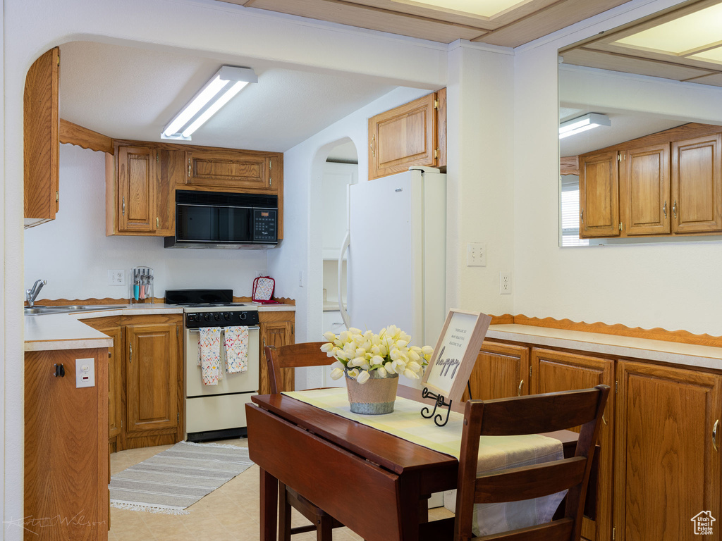 Kitchen with sink, light tile flooring, white fridge, and range