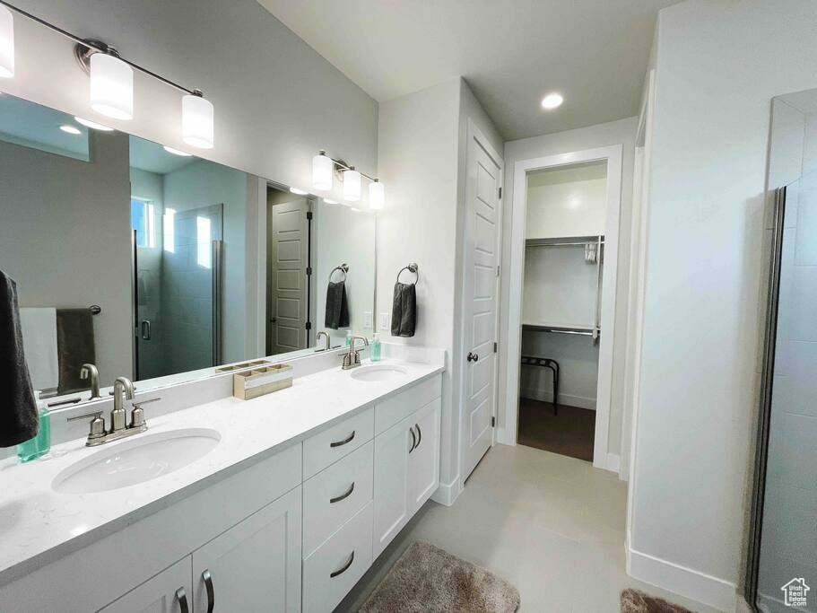 Bathroom featuring double sink, vanity with extensive cabinet space, and a shower with door