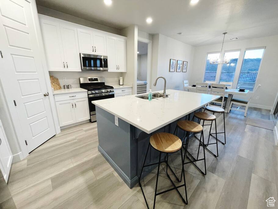 Kitchen with a kitchen breakfast bar, an island with sink, an inviting chandelier, light hardwood / wood-style flooring, and stainless steel appliances