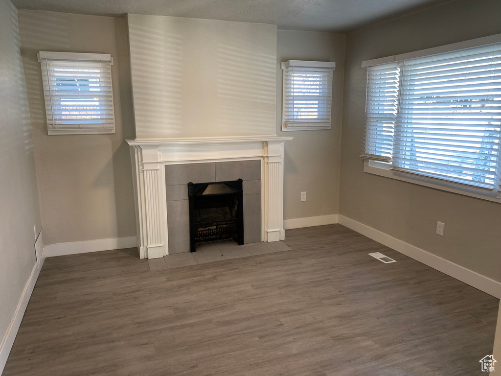 Unfurnished living room with plenty of natural light, dark hardwood / wood-style flooring, and a tiled fireplace