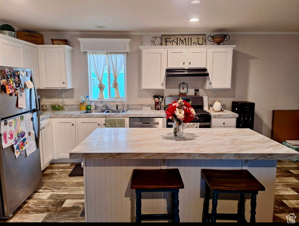 Kitchen with appliances with stainless steel finishes, white cabinets, a center island, and hardwood / wood-style floors