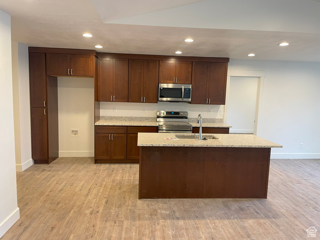 Kitchen with an island with sink, stainless steel appliances, sink, and light hardwood / wood-style flooring