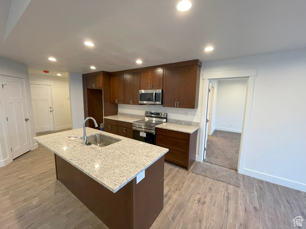 Kitchen featuring sink, appliances with stainless steel finishes, a center island with sink, light stone countertops, and light wood-type flooring