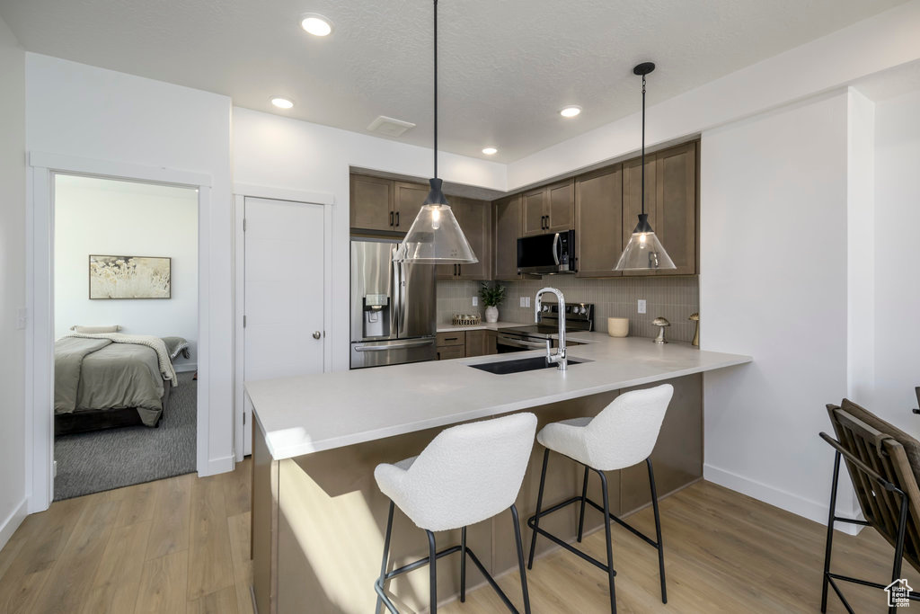 Kitchen with backsplash, light hardwood / wood-style floors, stainless steel appliances, and decorative light fixtures