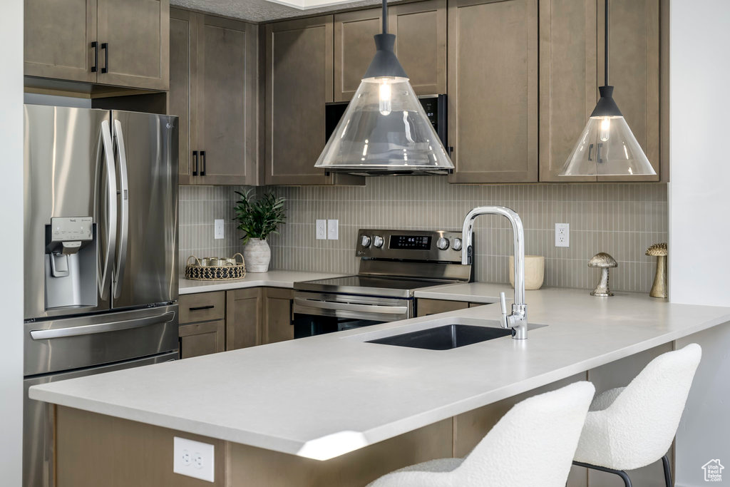Kitchen featuring tasteful backsplash, appliances with stainless steel finishes, a kitchen bar, and pendant lighting