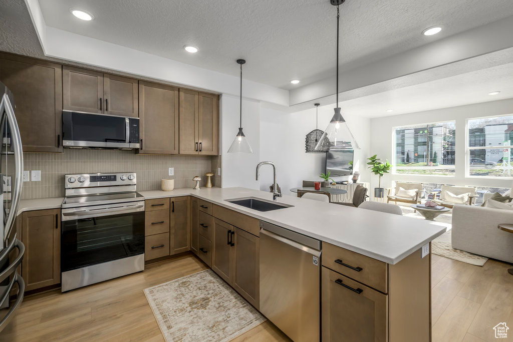 Kitchen with light wood-type flooring, stainless steel appliances, sink, hanging light fixtures, and tasteful backsplash