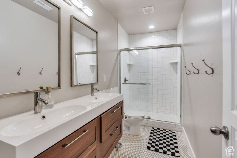 Bathroom featuring an enclosed shower, toilet, double sink vanity, and tile floors
