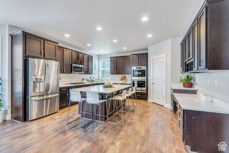 Kitchen featuring stainless steel appliances, light hardwood / wood-style floors, a breakfast bar, dark brown cabinets, and a center island