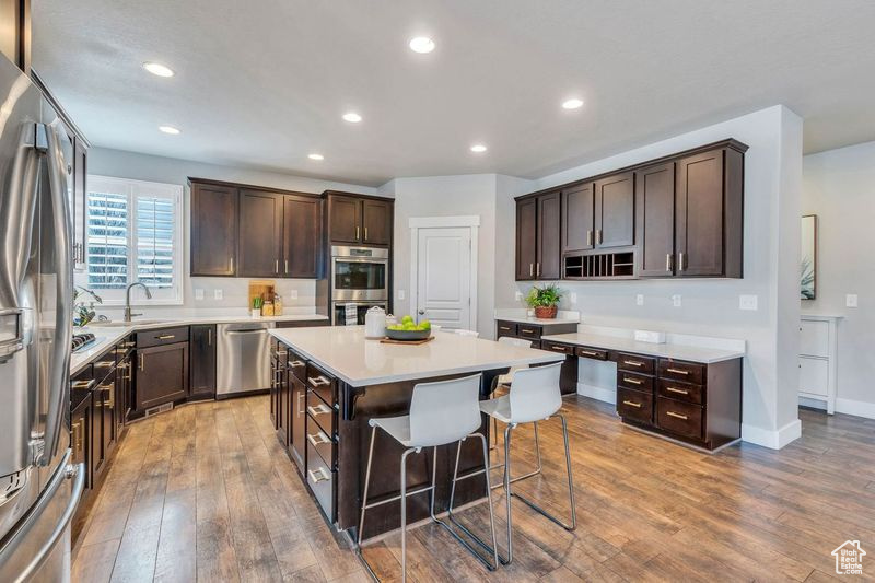 Kitchen featuring stainless steel appliances, light hardwood / wood-style flooring, a center island, and dark brown cabinets