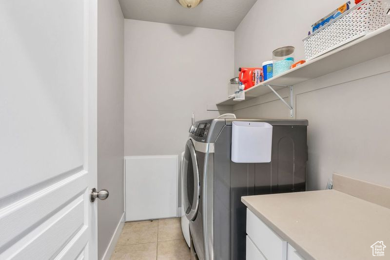 Laundry room featuring cabinets, washing machine and dryer, and light tile floors