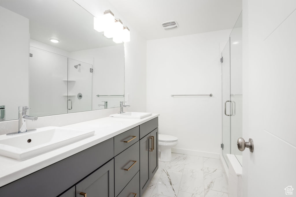 Bathroom featuring large vanity, a shower with door, tile floors, toilet, and double sink