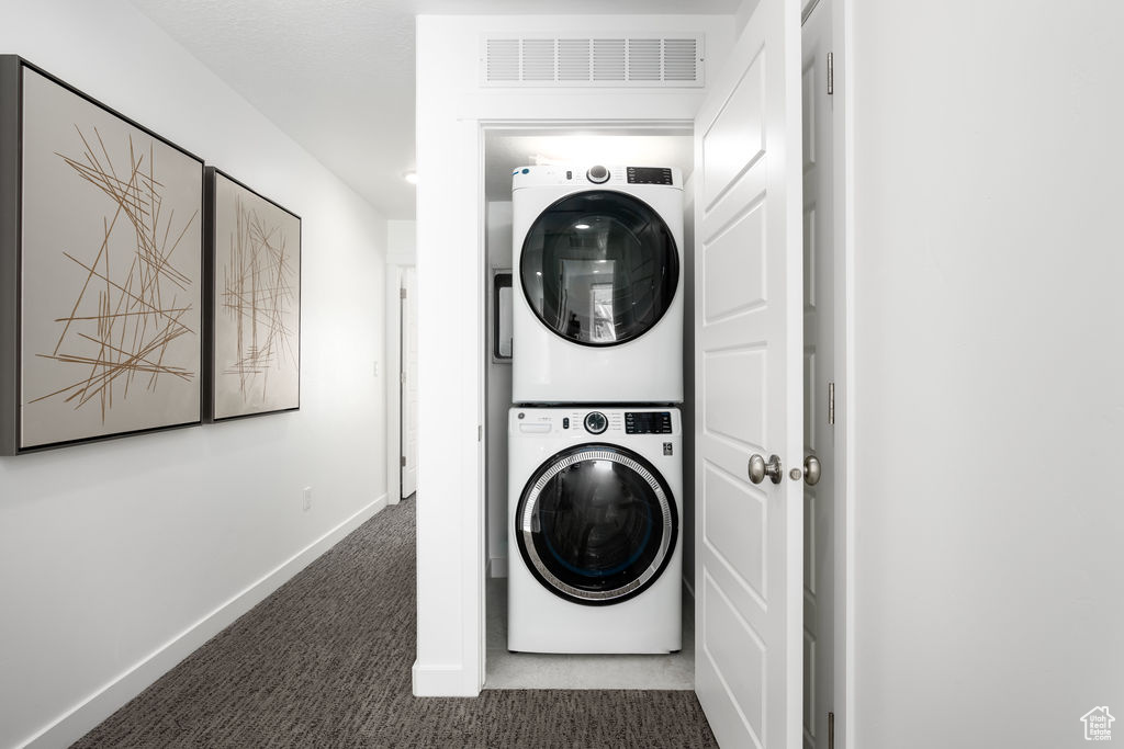 Clothes washing area with dark colored carpet and stacked washer / dryer