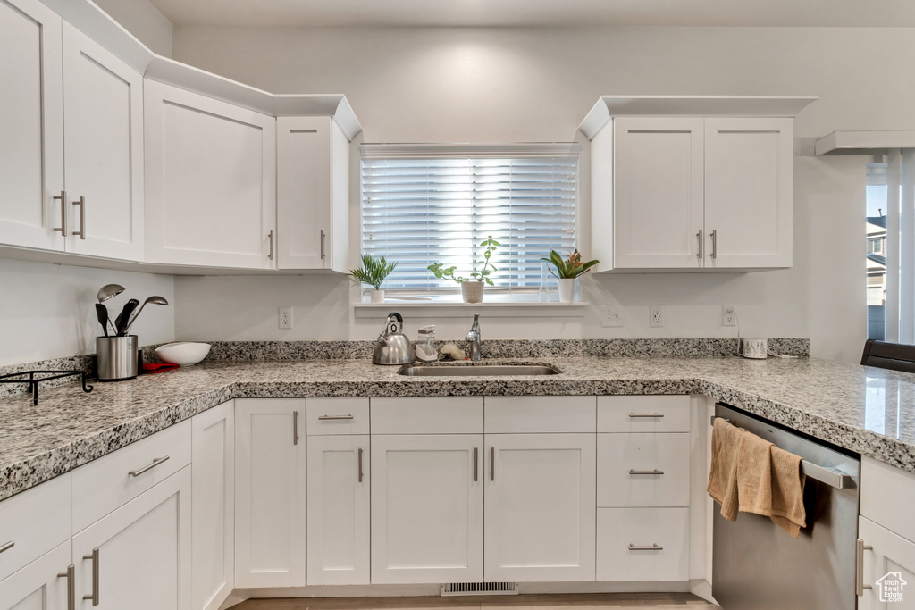 Kitchen featuring white cabinets, sink, dishwasher, and light stone countertops