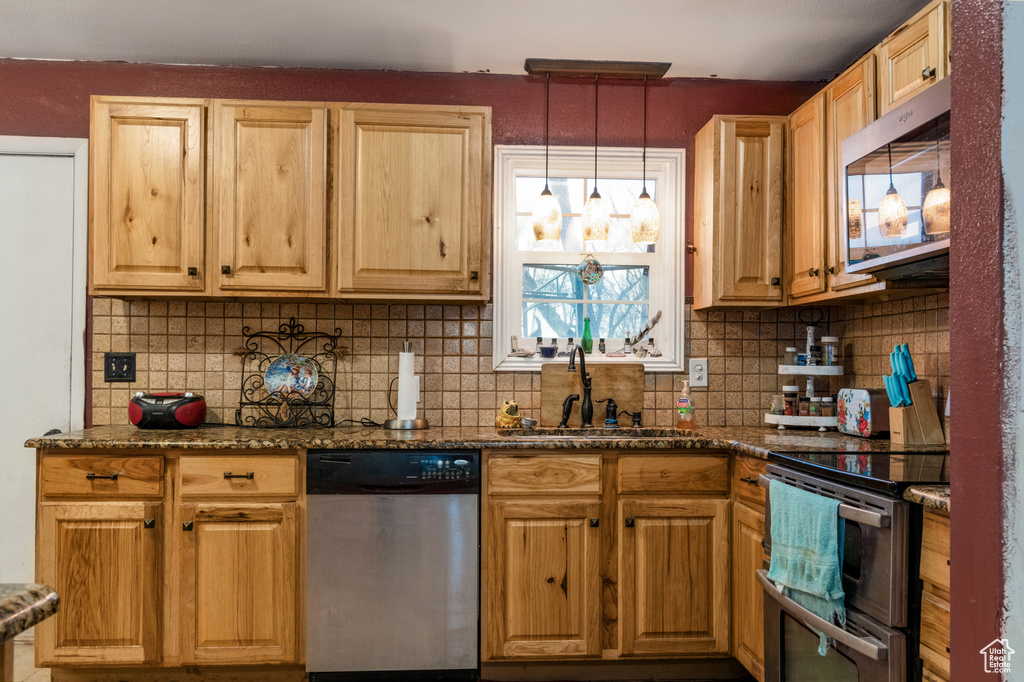 Kitchen featuring pendant lighting, stainless steel appliances, tasteful backsplash, and dark stone counters