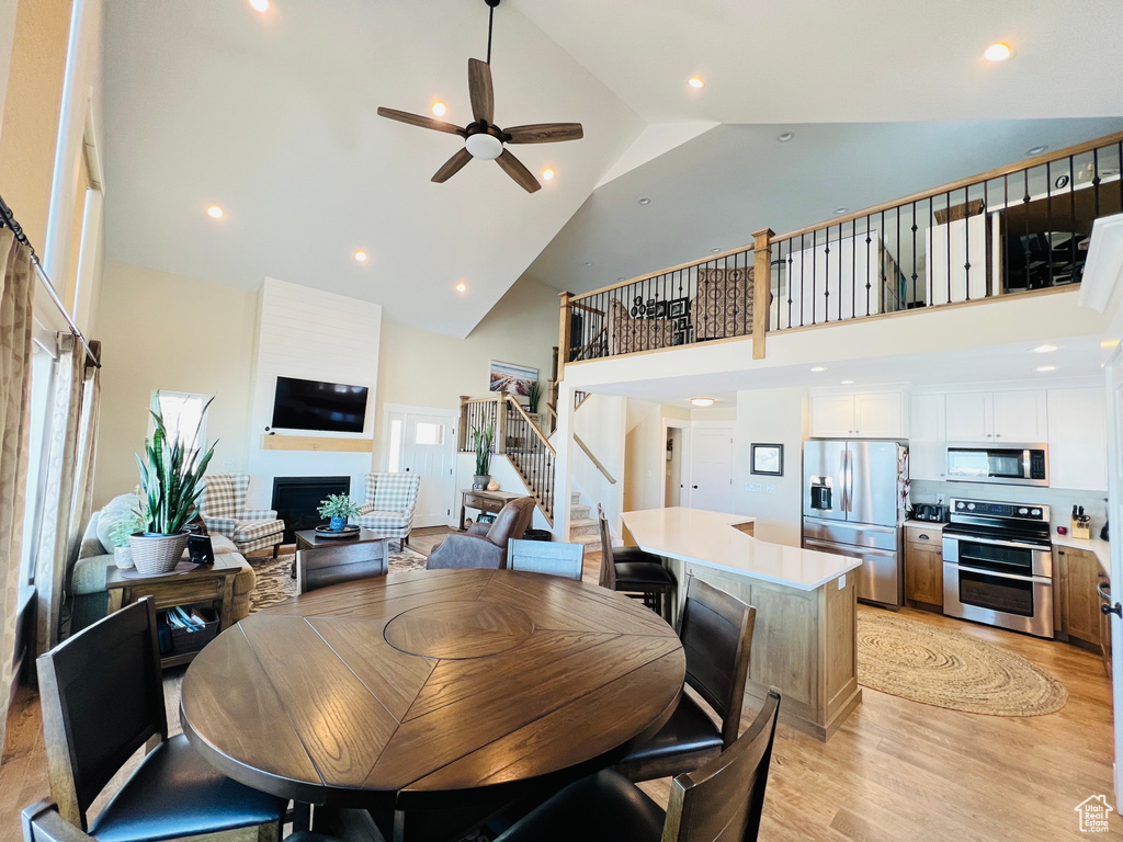 Dining space with light hardwood / wood-style flooring, ceiling fan, and high vaulted ceiling