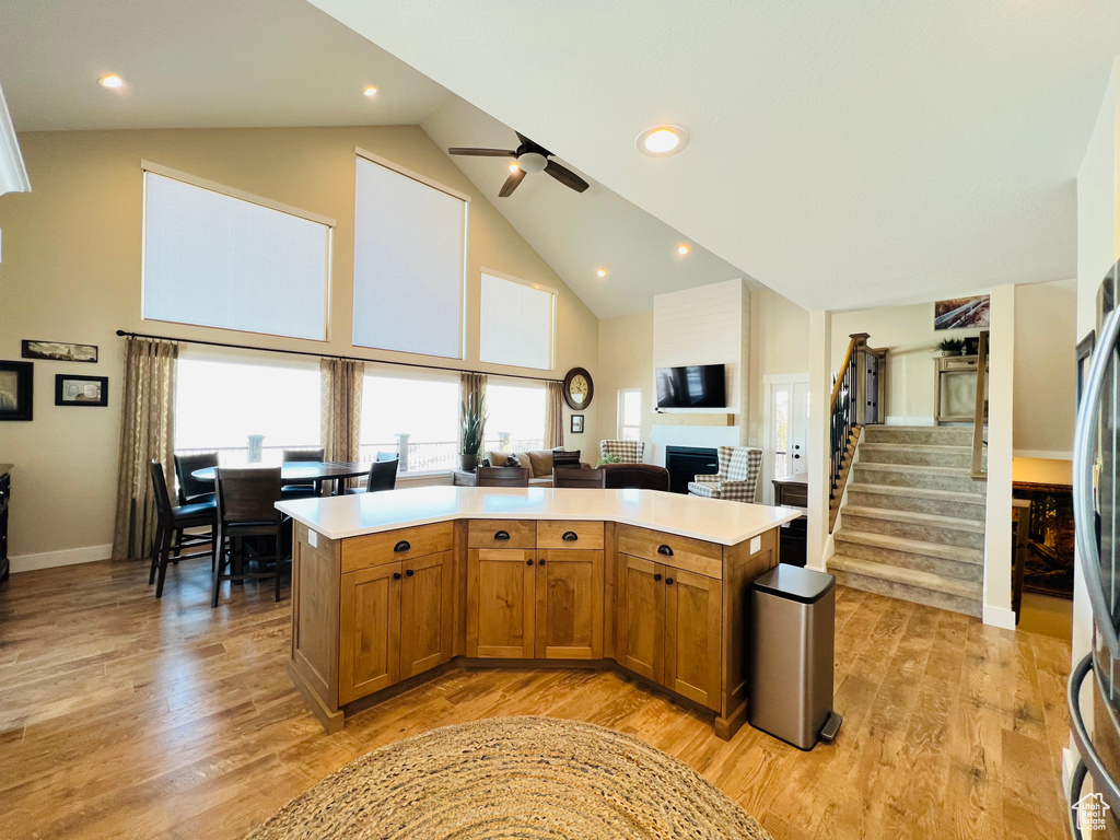 Kitchen with high vaulted ceiling, light hardwood / wood-style flooring, a kitchen island, and ceiling fan