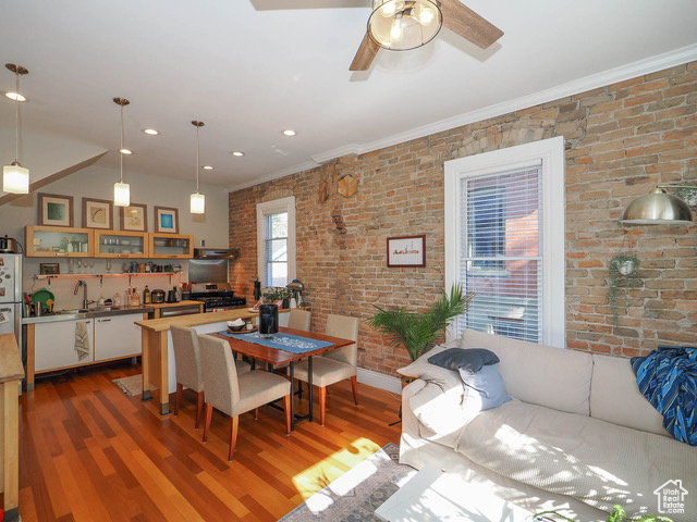 Dining area with ceiling fan, hardwood / wood-style flooring, ornamental molding, and brick wall
