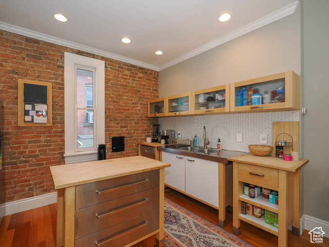 Kitchen with sink, dark wood-type flooring, brick wall, wood counters, and ornamental molding