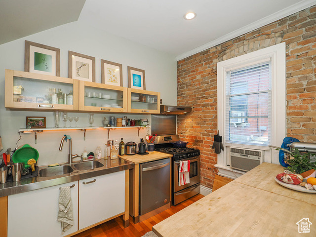 Kitchen with stainless steel dishwasher, stove, brick wall, and sink
