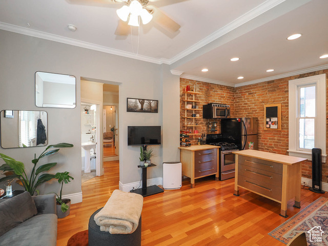 Living room with crown molding, brick wall, ceiling fan, and light hardwood / wood-style floors