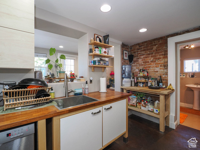 Kitchen with sink, plenty of natural light, white cabinets, and brick wall
