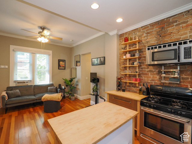 Kitchen featuring ceiling fan, brick wall, appliances with stainless steel finishes, wood counters, and wood-type flooring