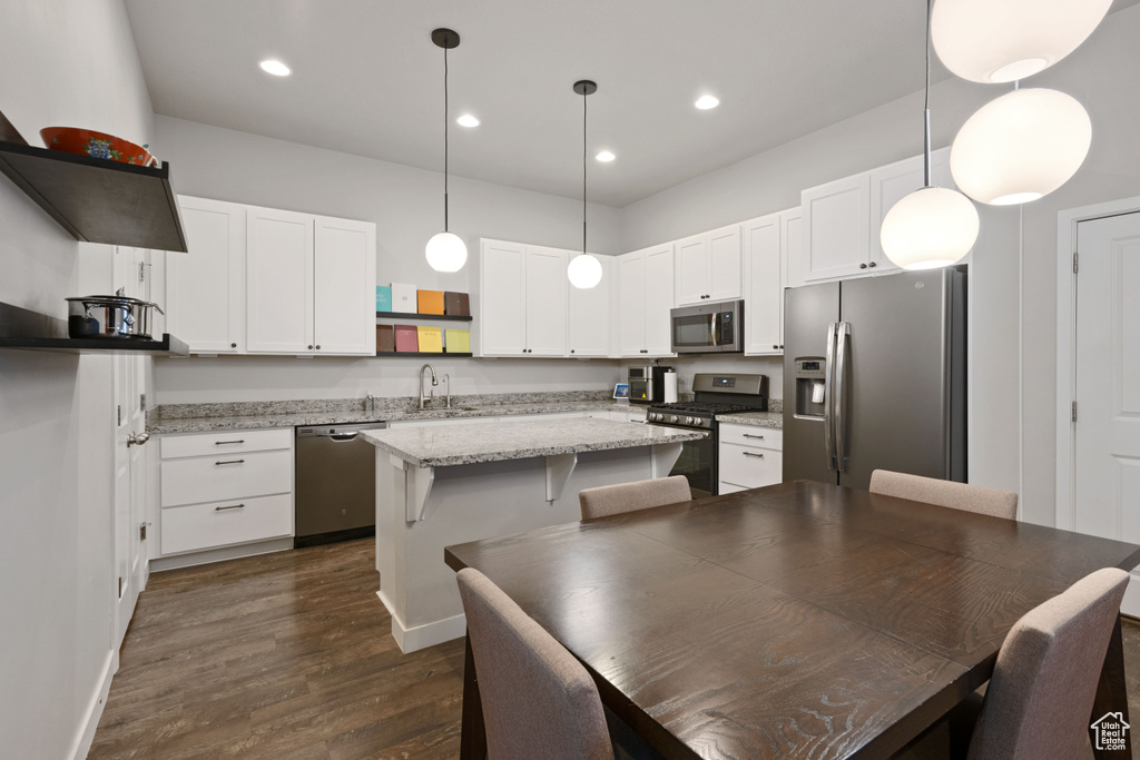 Kitchen with pendant lighting, stainless steel appliances, dark hardwood / wood-style flooring, and white cabinets